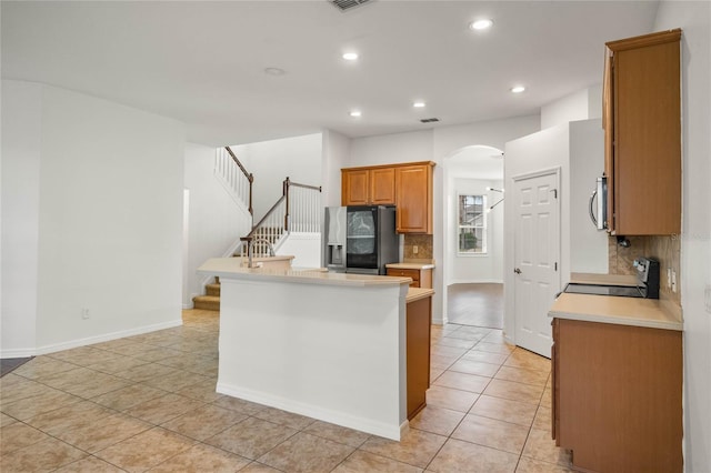 kitchen featuring a kitchen bar, decorative backsplash, refrigerator with ice dispenser, range, and light tile patterned flooring