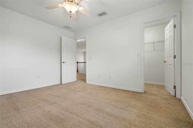 unfurnished bedroom featuring light carpet, a walk in closet, a closet, and ceiling fan