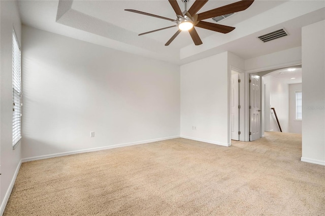 empty room featuring light carpet, a tray ceiling, and ceiling fan