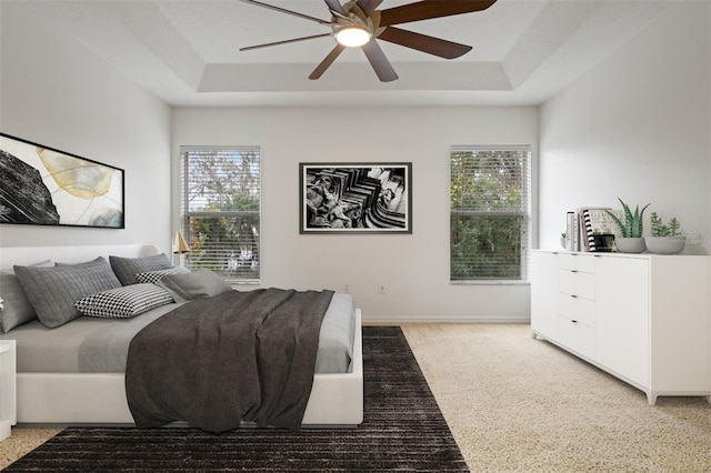 bedroom with a raised ceiling, multiple windows, and ceiling fan