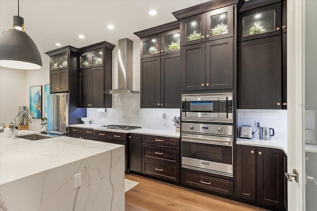 kitchen with sink, wall chimney exhaust hood, stainless steel appliances, decorative light fixtures, and light wood-type flooring