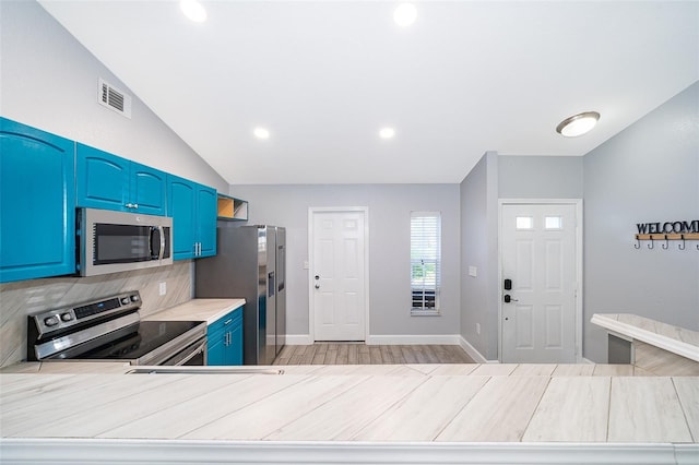 kitchen featuring blue cabinetry, light hardwood / wood-style floors, lofted ceiling, decorative backsplash, and appliances with stainless steel finishes