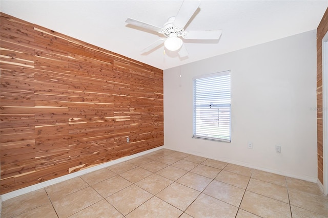 tiled empty room featuring ceiling fan and wood walls