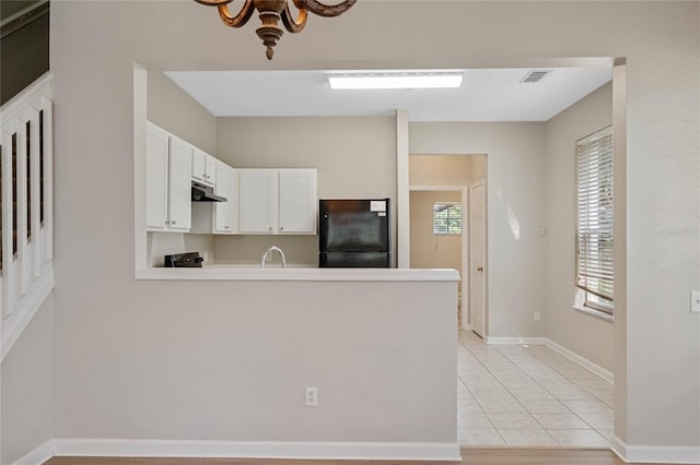 kitchen with kitchen peninsula, white cabinetry, black refrigerator, and light tile patterned flooring