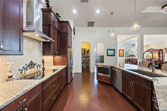 kitchen with a sink, visible vents, wall chimney range hood, appliances with stainless steel finishes, and dark wood finished floors