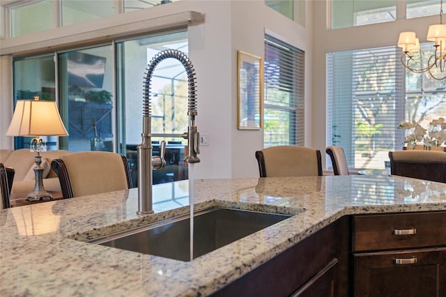 kitchen featuring light stone counters, dark brown cabinetry, a sink, and an inviting chandelier