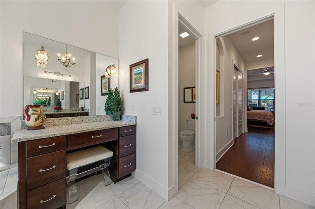 ensuite bathroom with baseboards, connected bathroom, toilet, marble finish floor, and vanity