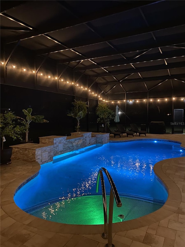 pool at night with glass enclosure, a patio area, and an outdoor pool