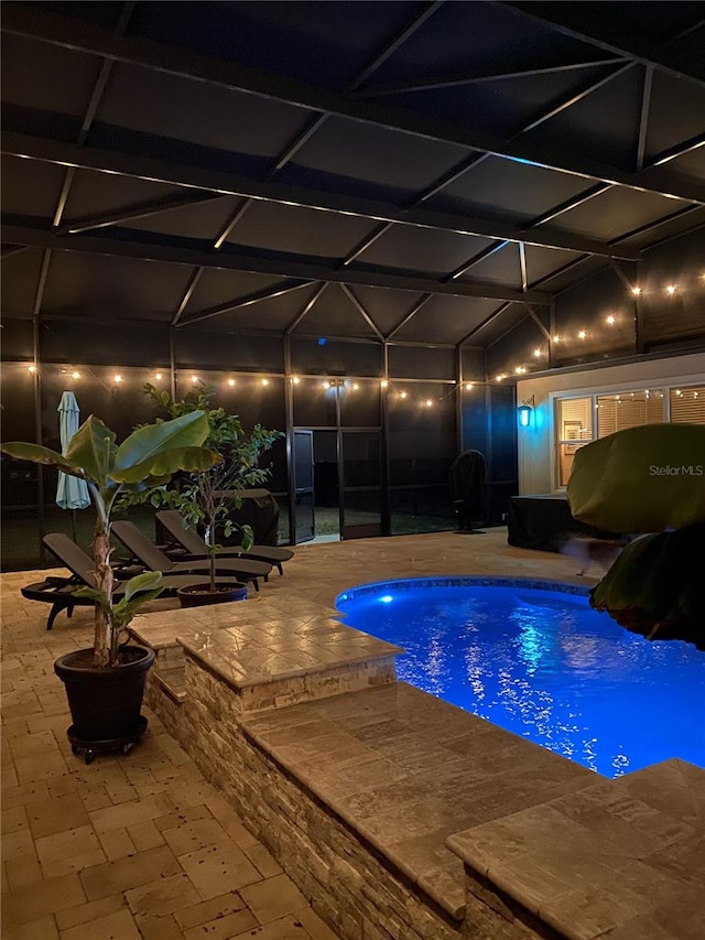 pool at night with an outdoor pool, glass enclosure, and a patio