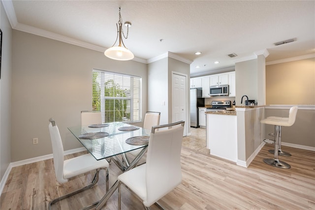 dining room featuring light hardwood / wood-style flooring, crown molding, and sink