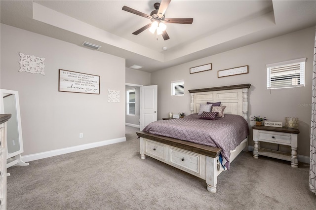 carpeted bedroom with ceiling fan, a raised ceiling, and multiple windows