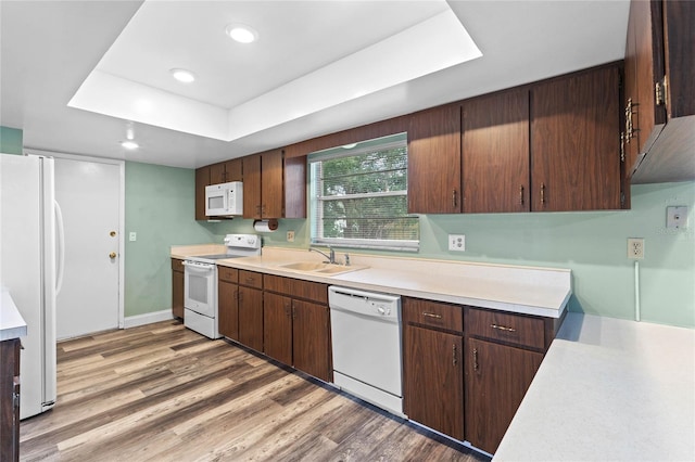 kitchen featuring white appliances, a tray ceiling, dark brown cabinetry, sink, and hardwood / wood-style floors