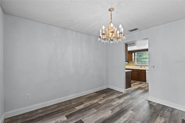 unfurnished dining area with a textured ceiling, dark hardwood / wood-style floors, an inviting chandelier, and sink