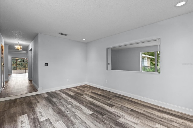 empty room with a chandelier, a textured ceiling, and hardwood / wood-style flooring