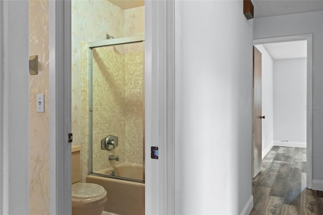 bathroom with toilet, wood-type flooring, and bath / shower combo with glass door