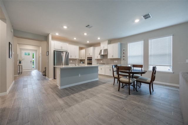 kitchen with white cabinets, a center island with sink, stainless steel refrigerator, and plenty of natural light