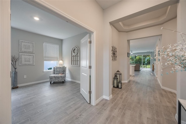 corridor with a tray ceiling and light hardwood / wood-style flooring