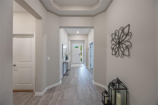 hall with a raised ceiling and light wood-type flooring