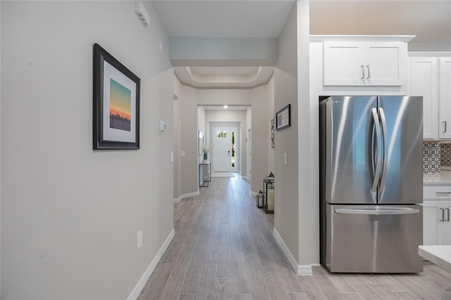 kitchen with a raised ceiling, light hardwood / wood-style flooring, decorative backsplash, stainless steel fridge, and white cabinetry