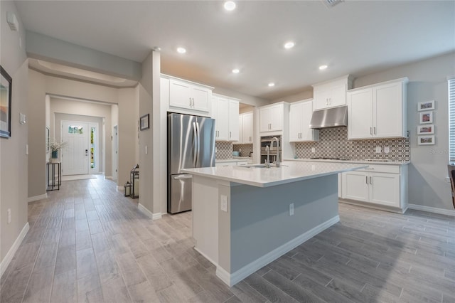 kitchen featuring white cabinets, light hardwood / wood-style flooring, stainless steel refrigerator, and a kitchen island with sink