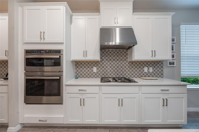 kitchen with white cabinets, appliances with stainless steel finishes, tasteful backsplash, and wall chimney range hood