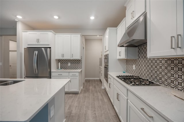 kitchen featuring appliances with stainless steel finishes, light wood-type flooring, light stone counters, sink, and white cabinets