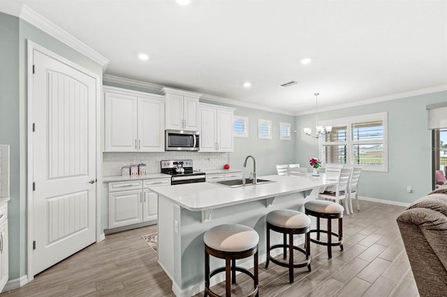 kitchen featuring appliances with stainless steel finishes, sink, pendant lighting, a center island with sink, and white cabinets