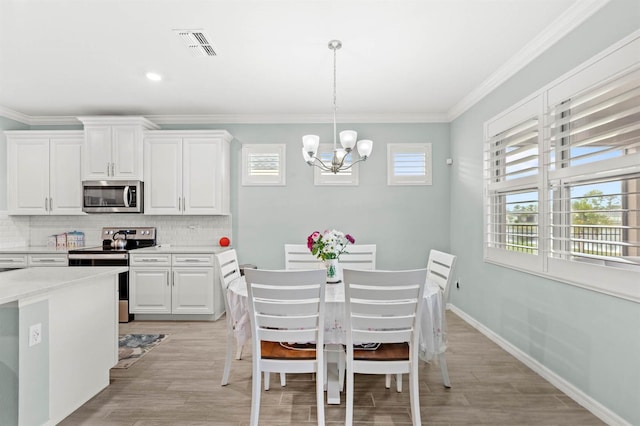 dining space with light hardwood / wood-style floors, ornamental molding, and an inviting chandelier