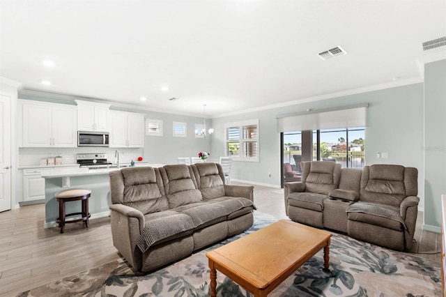 living room with light wood-type flooring, crown molding, and a notable chandelier