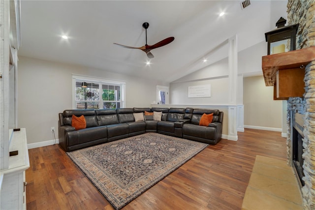 living room with ceiling fan, dark hardwood / wood-style flooring, a stone fireplace, and lofted ceiling