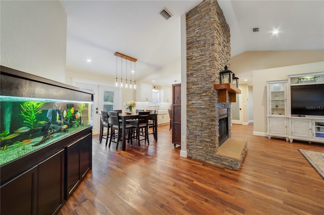 dining area with hardwood / wood-style flooring, a stone fireplace, and lofted ceiling