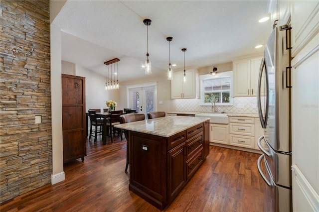 kitchen with pendant lighting, stainless steel fridge, a kitchen island, light stone counters, and a breakfast bar area