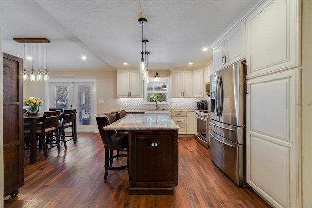 kitchen featuring pendant lighting, a kitchen breakfast bar, appliances with stainless steel finishes, a kitchen island, and light stone counters