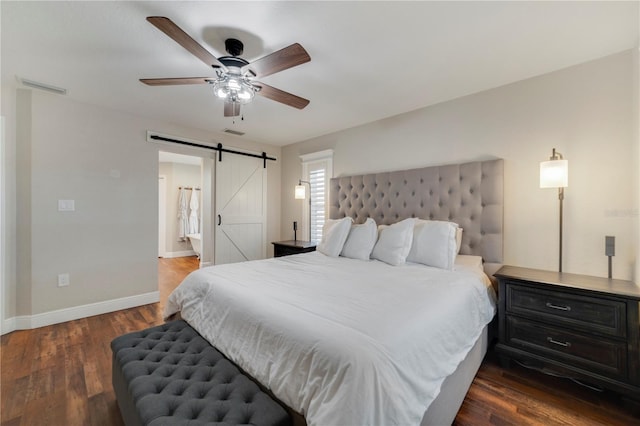 bedroom with connected bathroom, a barn door, ceiling fan, and dark hardwood / wood-style floors