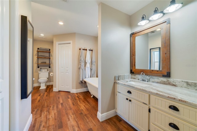 bathroom with a tub to relax in, vanity, wood-type flooring, and toilet