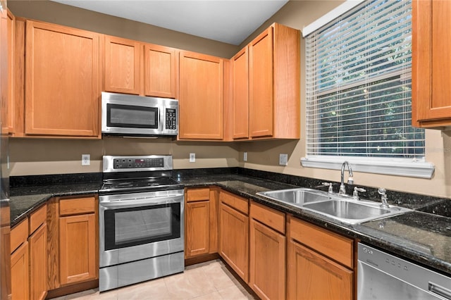 kitchen with dark stone countertops, sink, light tile patterned floors, and stainless steel appliances