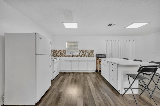 kitchen with decorative backsplash, a breakfast bar, hardwood / wood-style flooring, white fridge, and white cabinetry