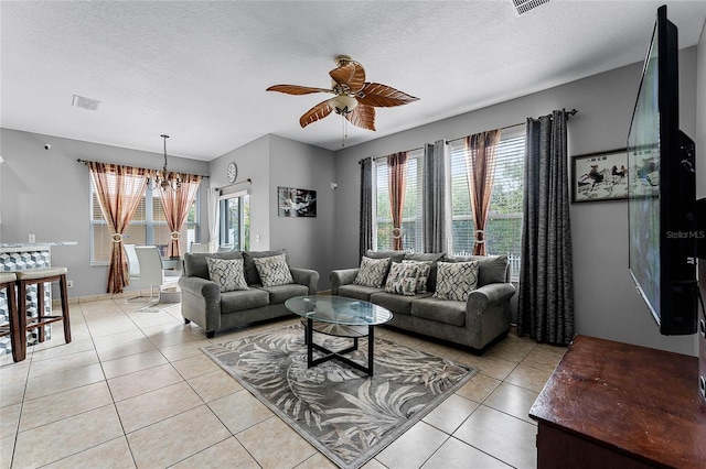 living room featuring ceiling fan with notable chandelier, a textured ceiling, a wealth of natural light, and light tile patterned flooring