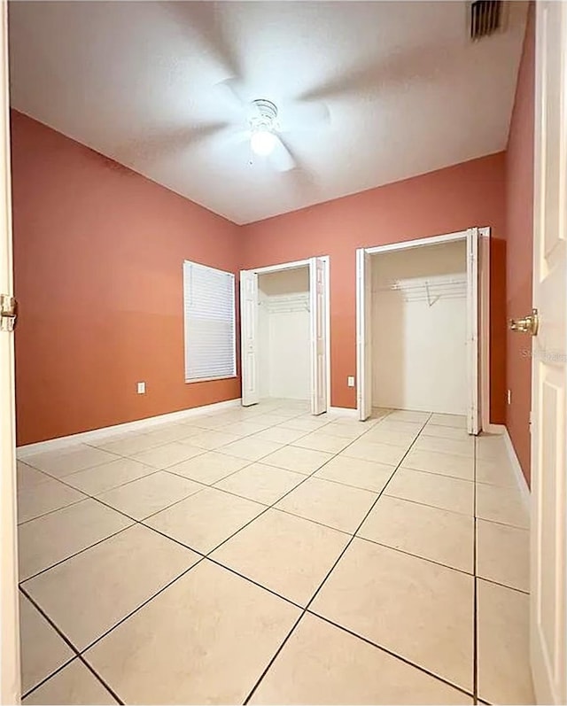 unfurnished bedroom featuring light tile patterned floors, multiple closets, and ceiling fan