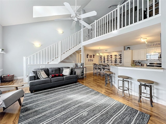 living room featuring a skylight, high vaulted ceiling, hardwood / wood-style flooring, and ceiling fan