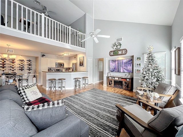 living room featuring high vaulted ceiling, light hardwood / wood-style floors, and ceiling fan with notable chandelier