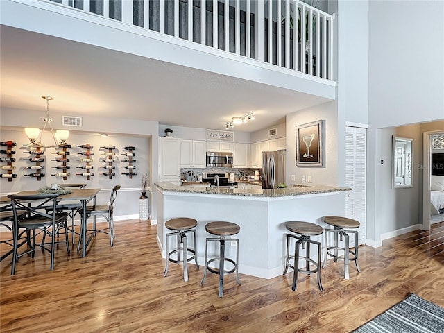 kitchen with light stone countertops, a towering ceiling, stainless steel appliances, white cabinets, and a chandelier