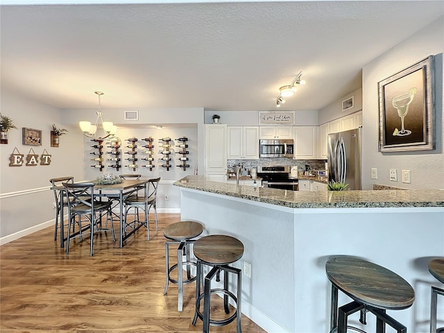 kitchen with white cabinets, appliances with stainless steel finishes, tasteful backsplash, decorative light fixtures, and a chandelier