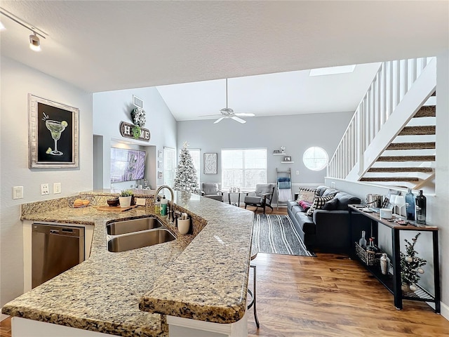 kitchen with stainless steel dishwasher, vaulted ceiling, ceiling fan, sink, and hardwood / wood-style flooring