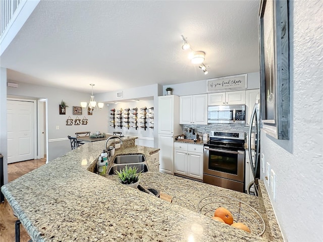 kitchen with sink, a notable chandelier, decorative backsplash, white cabinets, and appliances with stainless steel finishes