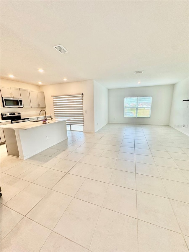 kitchen featuring light tile patterned floors, visible vents, appliances with stainless steel finishes, open floor plan, and a sink