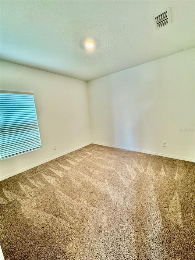 carpeted empty room featuring visible vents, a textured ceiling, and baseboards