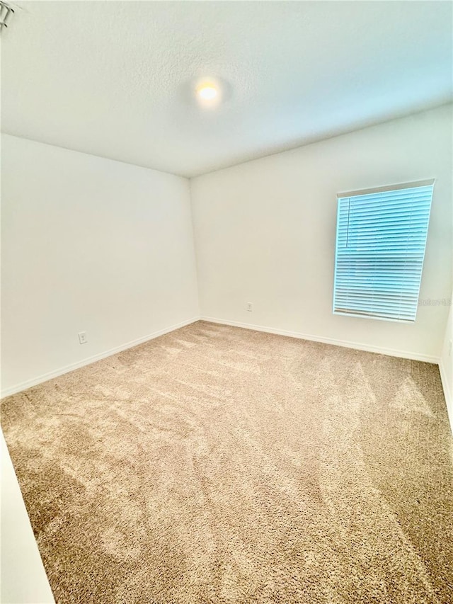 carpeted empty room with a textured ceiling and baseboards