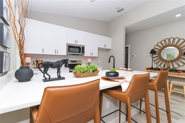 kitchen with a breakfast bar, lofted ceiling, light hardwood / wood-style flooring, appliances with stainless steel finishes, and white cabinetry