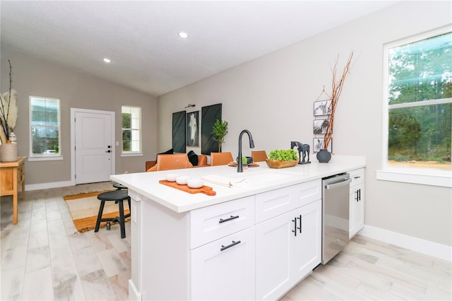 kitchen with light wood-type flooring, stainless steel dishwasher, vaulted ceiling, sink, and white cabinets